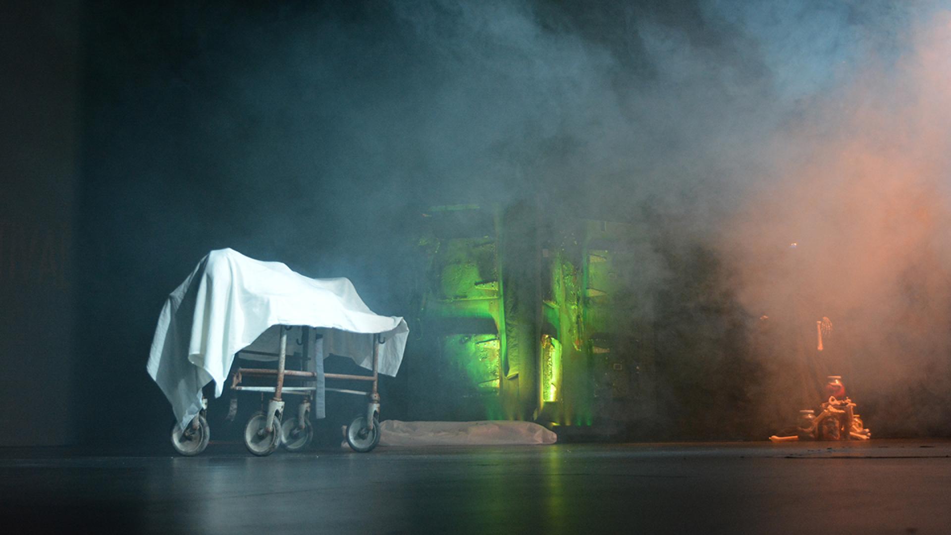Actor on a gurney covered with white sheet on stage with fog and smoke