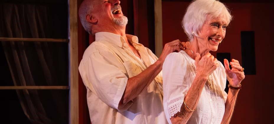 Senior man laughing and rubbing senior woman actress' shoulders on stage performing